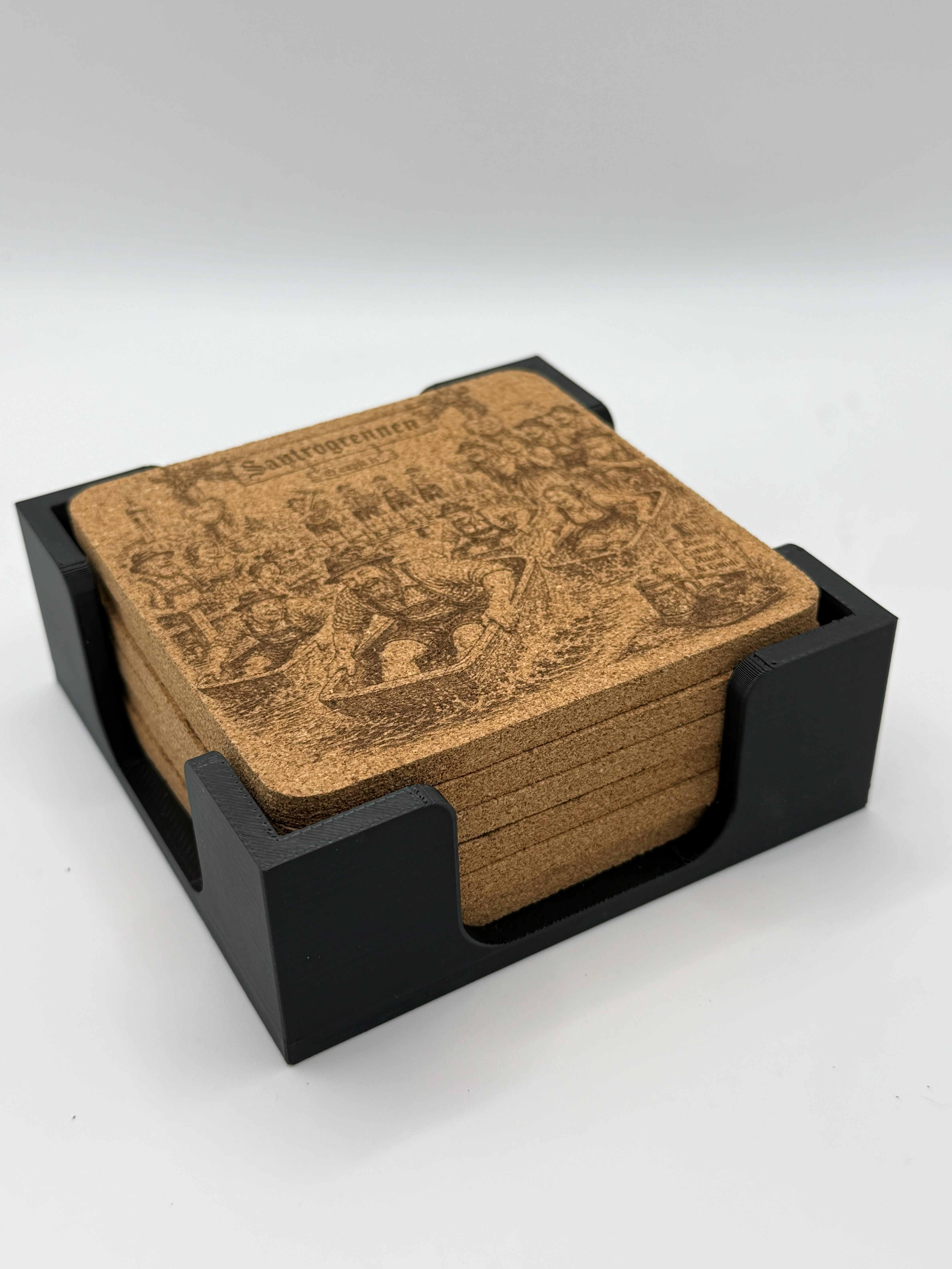 Gestapelte gravierte Korkbierdeckel im schwarzen 3D-gedruckten Halter, Schraegansicht des kompletten Sets