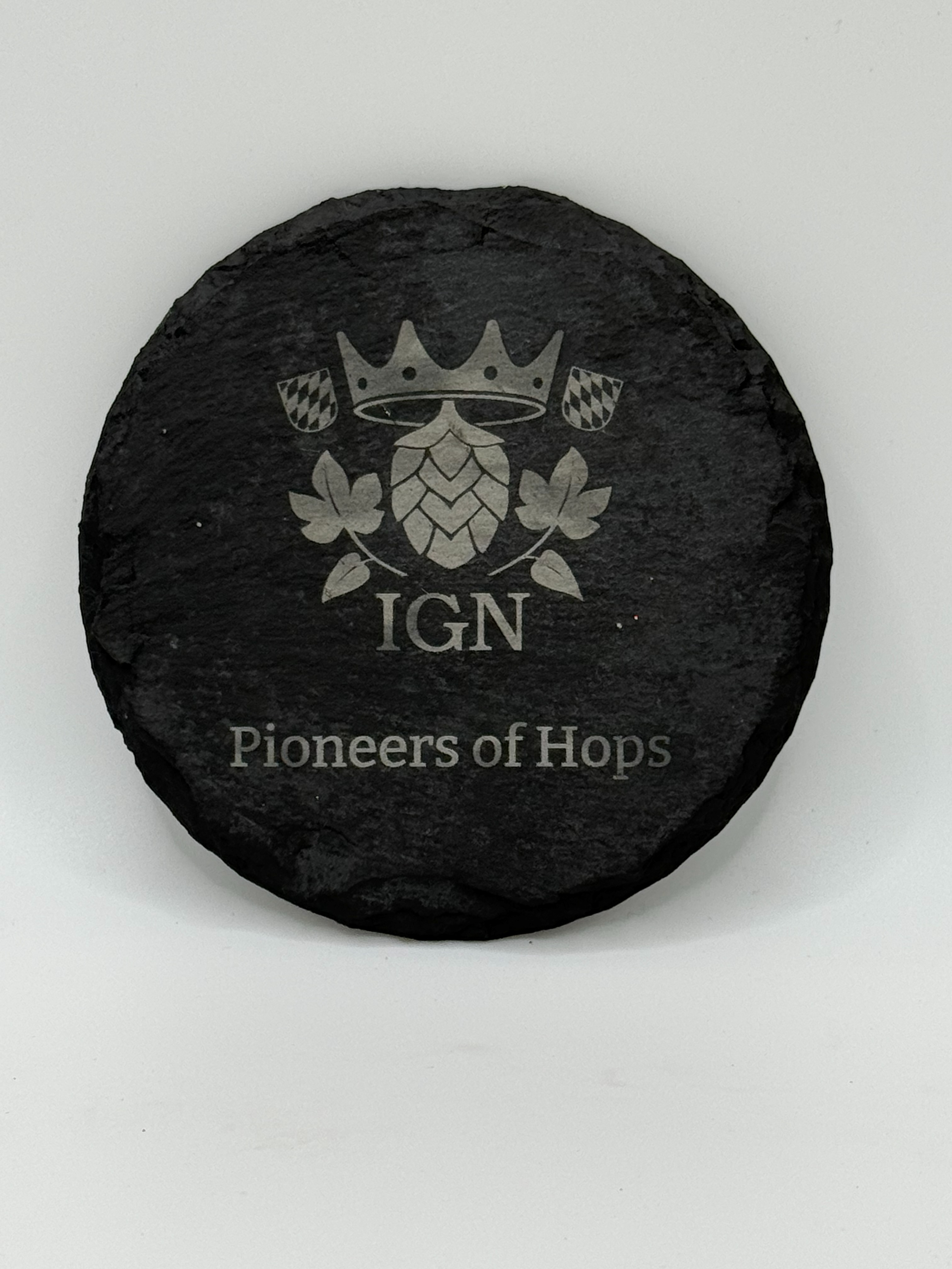 Runder Schieferuntersetzer mit lasergraviertem Firmenlogo IGN Qualitaetshopfen und Schriftzug "Pioneers of Hops" als Beispiel fuer eine Logogravur